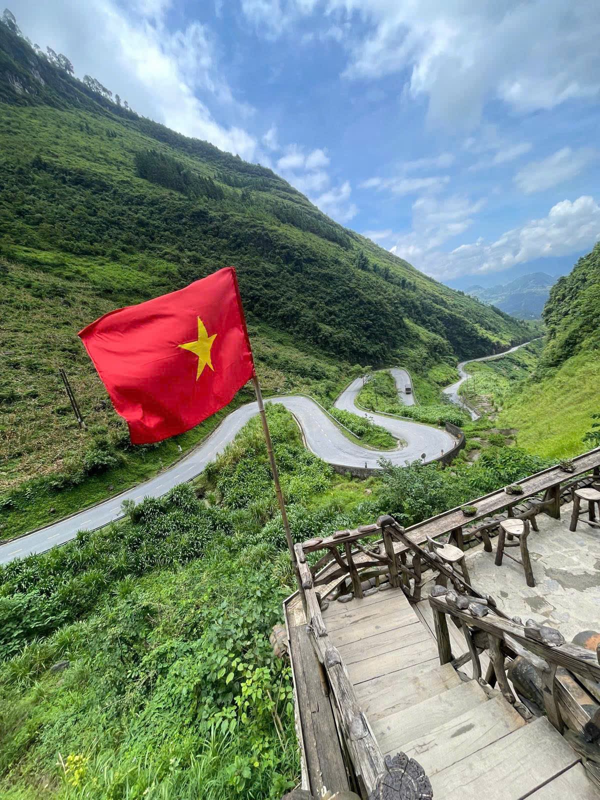 A Vietnamese flag above a winding mountain road in Ha Giang