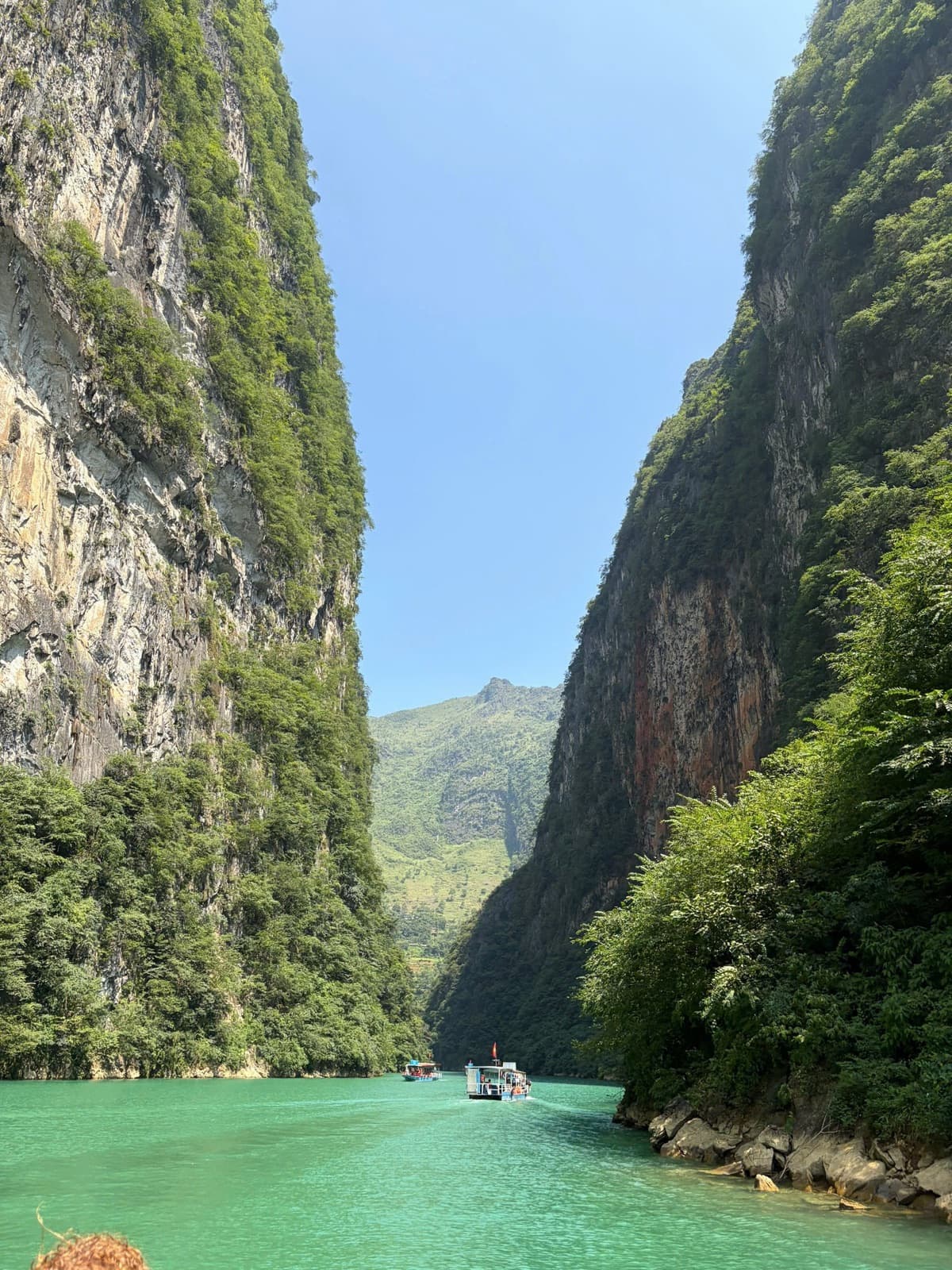 A boat on the emerald Nho Que River between towering cliffs