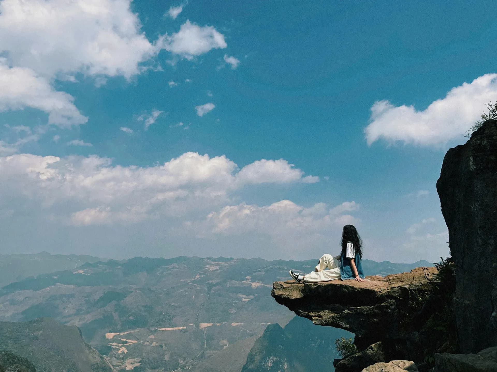 A traveller sitting on a cliff edge above the Ha Giang valleys